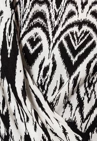 Czarna i biała tkanina z wyrazistym, abstrakcyjnym wzorem zawierającym motywy zygzaków i fal. Tekstura wydaje się gładka z lekkim połyskiem.