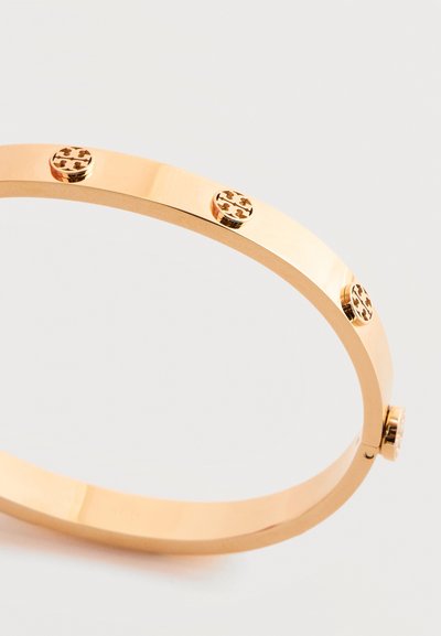 Βραχιόλι βέργας από μέταλλο σε χρυσό τόνο με στρογγυλές διακοσμητικές βίδες διατεταγμένες ομοιόμορφα στην επιφάνειά του σε λευκό φόντο.