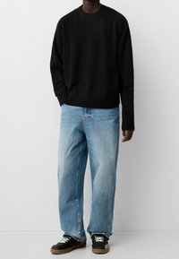 Pull en maille texturée noire, coupe décontractée, associé à un jean bleu clair ample et des baskets noires avec des semelles beige.