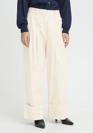 Wide-leg cream trousers with rolled cuffs worn with a navy long-sleeve top and black pointed-toe heeled shoes.