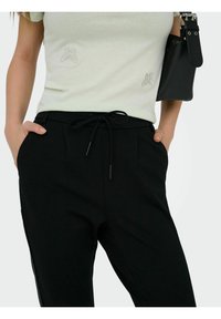 Lys grønn t-skjorte med broderte sommerfugldesign på brystet, kombinert med svarte bukser med snøring og sidelommer.