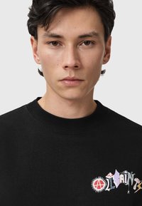 Sudadera negra con cuello redondo, con estampados gráficos coloridos en el pecho y una tela suave y texturizada.