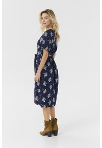 Marinblå blommig klänning med korta ärmar, bälte i midjan och knälång längd. Ett par tanfärgade mockaboots med blockklackar kompletterar stilen.