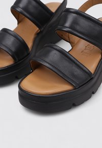 Sandalias de plataforma negras con dos correas anchas, hechas de cuero suave. La plantilla es de color marrón claro y la suela presenta un diseño texturizado y grueso.