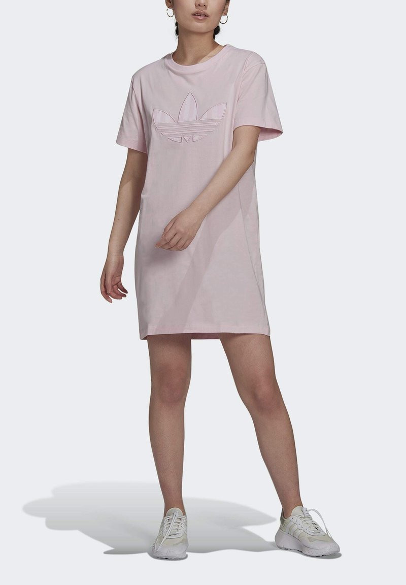 Růžové šaty s krátkým rukávem vyrobené z bavlny, s tónovým logem Adidas na hrudi. Design je volného střihu s rovnou siluetou.