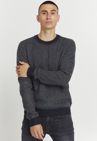 Marineblå strikket sweater med et struktureret mønster, ribbede manchetter og rund hals. Har en tætsiddende silhuet. Bæres med mørke jeans.