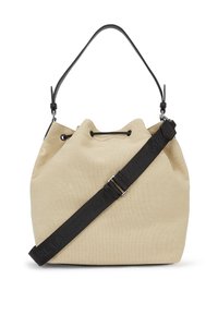 Beige canvas bucket bag with a drawstring closure and a black adjustable strap. Features subtle branding on the strap and a soft texture.