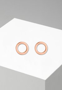 Rožinės aukso apvalūs auskarai su blizgiu paviršiumi, turintys lygų tekstūrą ir paprastą, švarią dizainą. Be jokių papildomų akcentų ar raštų.