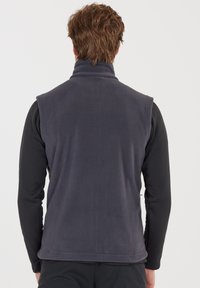 Fleece vest i mørkegrå, har høj krave, ærmeløst design, blød tekstur og flade sømme. Bæres over en sort langærmet skjorte.