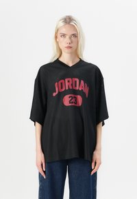 Maillot en maille noire avec une coupe ample, en V, à manches courtes. L'avant présente le texte "JORDAN" en rouge vif et le numéro "23" dans un design ovale.