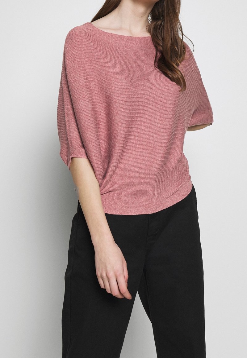 Kortärmad, löst sittande topp i strukturerad rosa stickad tyg; har en vid halsringning och en lätt fåll med subtila horisontella linjer.