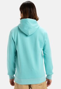 Sudadera turquesa con bolsillo canguro y capucha con cordón. Fabricada en tela suave, presenta puños acanalados y dobladillo para un ajuste ceñido.