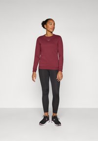 Bordeaux langermet genser med rund hals og broderte detaljer, kombinert med svarte leggings og svarte joggesko.