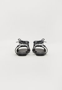 Mustad mustad sandaalid õhukeste rististe rihmadega ja lihtsa, minimalistliku disainiga. Tekstuuriga tald, ilma nähtavate riistade või aktsentideta.