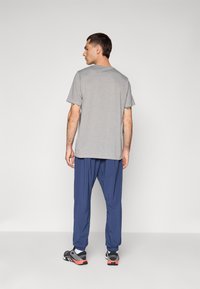 Gray short-sleeve t-shirt with a relaxed fit, paired with loose-fitting navy pants and black sneakers with red accents.