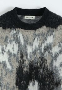 Pull en tricot noir, gris et blanc avec une finition texturée et duveteuse. Présente un col rond côtelé noir et un motif abstrait sur l'ensemble.
