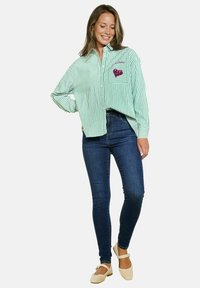 Groen en wit gestreepte overhemd met lange mouwen en een zak met een roze pailletten hart. Gecombineerd met donkere skinny jeans.