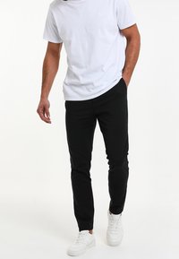 Black tapered jogger pants with pockets, crafted from a soft fabric, paired with a plain white T-shirt and white sneakers.