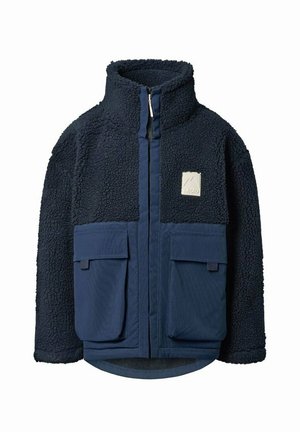 Giacca in pile blu navy con colletto alto, cerniera frontale, due grandi tasche frontali con patta e una piccola toppa chiara sul petto.