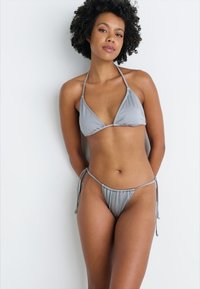 Γκρι μπικίνι με τριγωνικό τοπ και ρυθμιζόμενα ελαστικά πλαϊνά. Λείο ύφασμα, ελάχιστη κάλυψη και κομψός σχεδιασμός.
