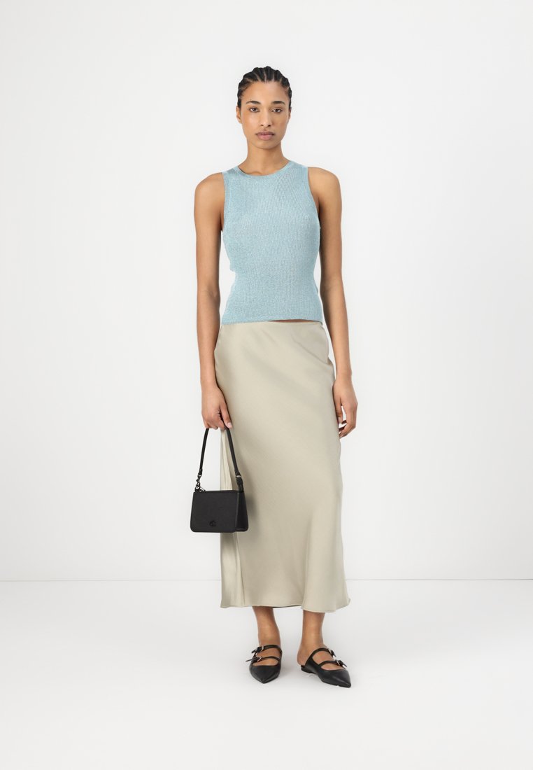 Débardeur en tricot côtelé bleu clair associé à une longue jupe beige, un sac à main noir et des ballerines noires avec des accents en forme de nœud.