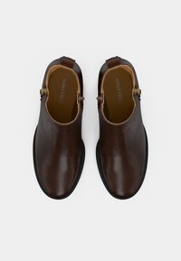 Brūnas ādas potīšu zābaki ar spīdīgu apdari, sānu rāvējslēdzējiem un melnām gumijas zolēm. Raksturo gluda tekstūra un apaļš purngals.