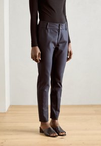 Navy trousers with a slim fit, two-button closure, and side pockets, paired with black slide sandals and a black long-sleeve top.