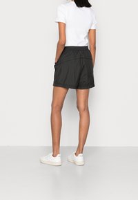 Czarne sportowe spodenki z elastycznym pasem, bocznymi kieszeniami i gładkim, lekkim materiałem, zestawione z białymi casualowymi trampkami.