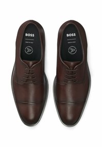 Scarpe da uomo in pelle marrone scuro con una finitura liscia, caratterizzate da un design con lacci, punta rotonda e dettagli di cucitura sottili.