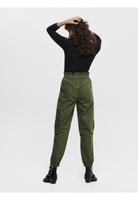 Gröna cargo-byxor med elastisk midja, ankle cuffs och sidofickor, tillsammans med en åtsittande svart långärmad topp.