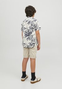Camicia bianca a maniche corte con stampa a foglie navy; pantaloni corti beige arrotolati; calze nere; scarpe casual con dettagli crema e navy.