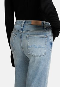 Jeans in denim azzurro chiaro con due tasche posteriori, caratterizzati da un sottile dettaglio di cucitura. Indossati con un top nero a maniche lunghe e a coste.