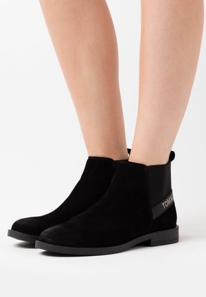 Black suede ankle boots with elastic side panels, rounded toes, flat black rubber soles, and a tonal logo accent on the side.