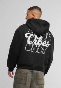 Felpa con cappuccio nera con una grande grafica bianca sul retro con la scritta "Good Vibes Only". Realizzata in un tessuto morbido e texturizzato.