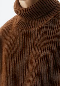 Hnědý rolák s žebrovaným vzorem, který má silný límec, strukturovaný pletený vzor a volný střih, zdůrazňující teplo a pohodlí.