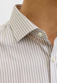 Chemise à rayures avec col boutonné. Présente des rayures étroites marron et blanches, un tissu lisse et un bouton unique au col.