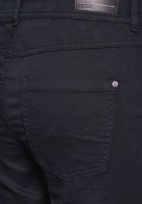 Granatowe dżinsy z tylną kieszenią z metalowymi nitami. Gładka tekstura z podwójnym ściegiem wzdłuż szwów.