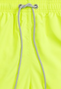 Neon żółte kąpielówki z elastycznym pasem i srebrnym sznurkiem. Gładki, lekki materiał z marszczeniem w pasie.