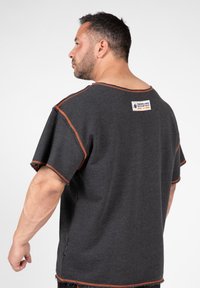 Grijze t-shirt met korte mouwen, voorzien van contrasterende oranje stiksels langs de halslijn en de zoom, en een klein label op de achterkant.
