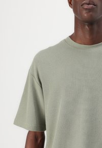 Grön texturerad T-shirt med rund hals och korta ärmar, som har en avslappnad passform och ribbat tyg.