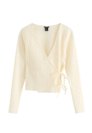 Kremfarvet tekstureret omslagsstriktrøje med lange ærmer og bindelukninger i siderne på en hvid baggrund.