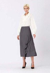 Blouse blanche à volants avec des manches ballons associée à une jupe grise à rayures verticales dotée d'un volan diagonal. Escarpins noirs à talons hauts.