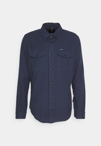 Camicia a maniche lunghe navy realizzata in tessuto testurizzato, con chiusura a bottone, due tasche sul petto e un orlo leggermente curvo.