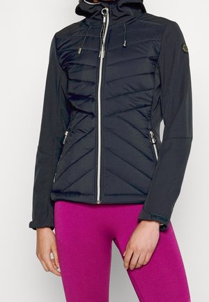 Schwarze gesteppte Jacke mit Reißverschluss und Kapuze, Reißverschlusstaschen und verstellbaren Bündchen, getragen zu leuchtend pinken Leggings.