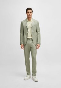 Light green suit with a textured finish, single-breasted jacket, and matching trousers. Paired with a cream polo and white sneakers.