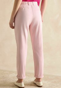 Gaiši rozā bikses ar brīvu piegriezumu, ar arku apakšā un diviem aizmugures kabatām. Gluda auduma virsma ar nelielu spīdumu.