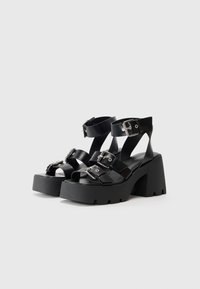 Sandalias de plataforma negras con correas anchas y hebillas ajustables. Presentan un tacón robusto y una suela de goma con relieve para una mayor tracción.