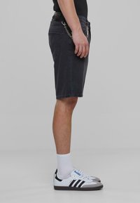 Zwarte denim shorts met een rechte pasvorm, zijzakken en kettingdetail, gecombineerd met wit-zwart sneakers en witte crew-sokken.