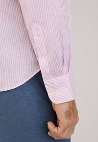 Lichtroze en witte gestreepte langarmshirt met een knoopsluiting bij de manchetten. Het shirt heeft een zachte textuur en een afgeronde zoom, gecombineerd met donkerblauwe broek.
