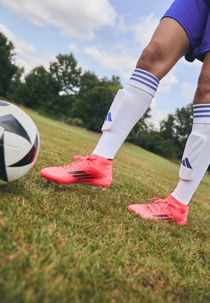 Fodboldspiller iført lyserøde fodboldstøvler, hvide sokker og blå shorts, som gør sig klar til at sparke til en sort-hvid fodbold på en græsmark.